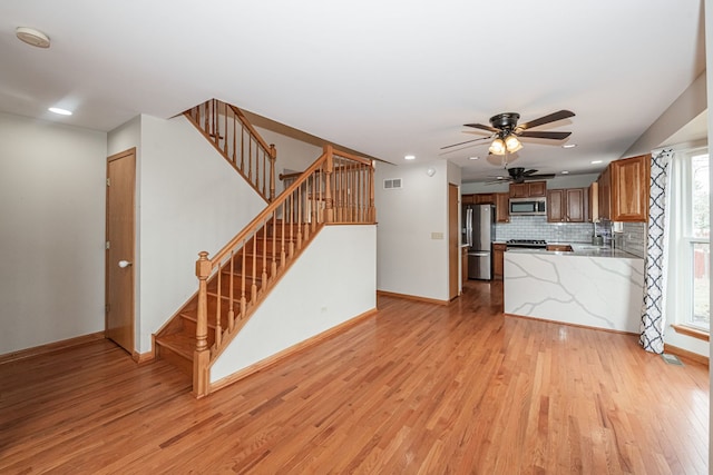 kitchen featuring stainless steel appliances, kitchen peninsula, decorative backsplash, and light wood-type flooring