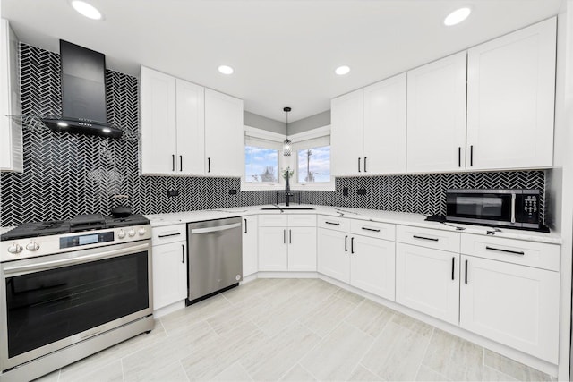 kitchen featuring decorative light fixtures, white cabinetry, sink, stainless steel appliances, and wall chimney range hood