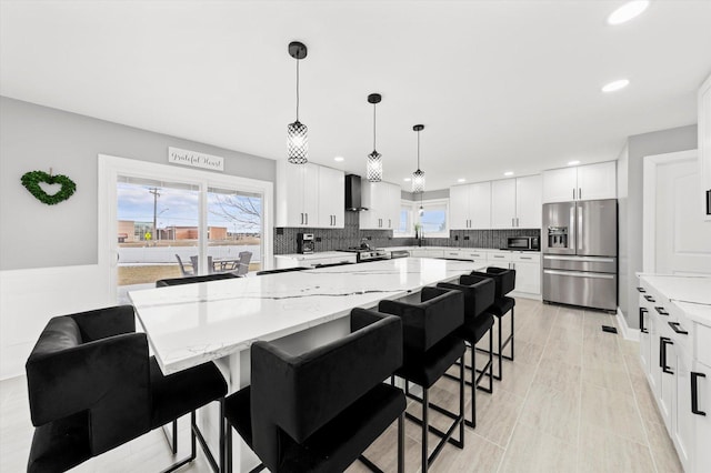 kitchen with white cabinetry, a kitchen island, pendant lighting, stainless steel appliances, and wall chimney range hood