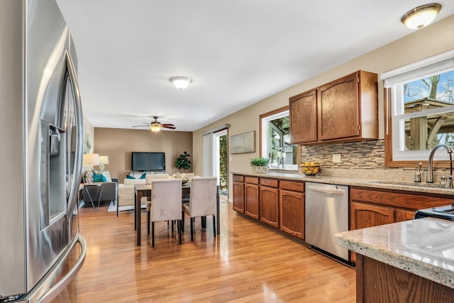 kitchen featuring appliances with stainless steel finishes, light wood-type flooring, ceiling fan, decorative backsplash, and sink