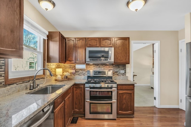 kitchen with light stone countertops, stainless steel appliances, light wood-type flooring, backsplash, and sink