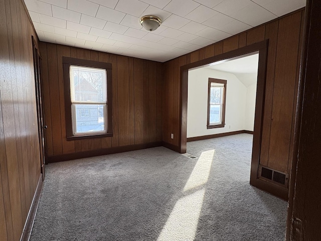 carpeted empty room featuring wood walls