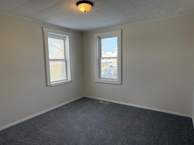 empty room with ornamental molding, plenty of natural light, and dark carpet