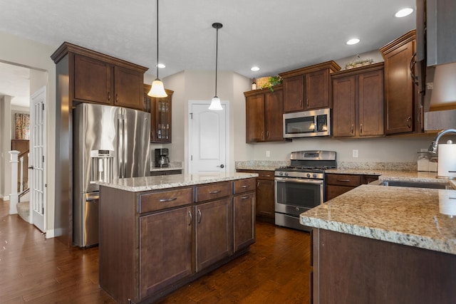 kitchen featuring pendant lighting, sink, stainless steel appliances, a kitchen island, and dark brown cabinetry