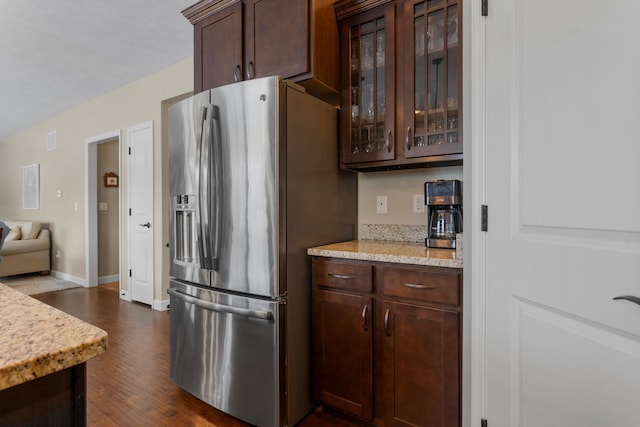 kitchen with light stone counters, dark wood-type flooring, stainless steel fridge with ice dispenser, and dark brown cabinetry