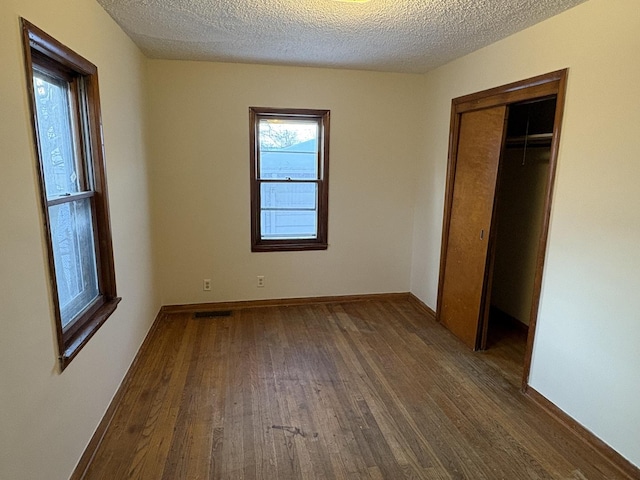 unfurnished bedroom with a closet, dark hardwood / wood-style flooring, and a textured ceiling