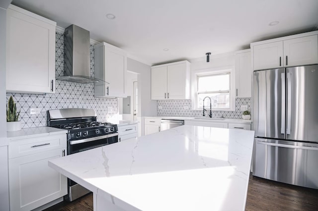 kitchen featuring wall chimney exhaust hood, a center island, white cabinetry, appliances with stainless steel finishes, and sink