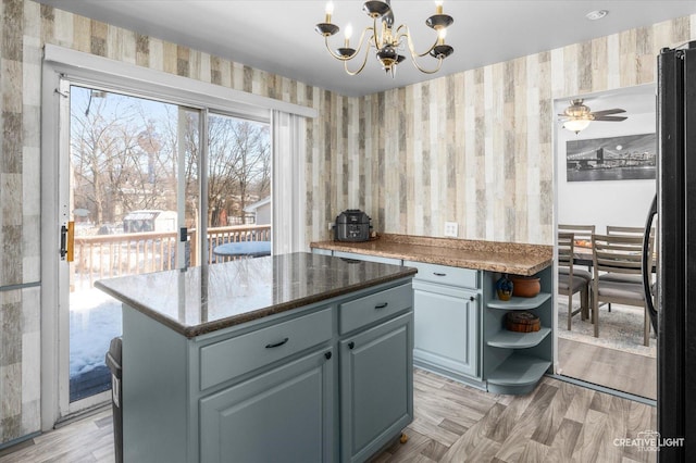 kitchen featuring decorative light fixtures, black fridge, light hardwood / wood-style flooring, ceiling fan with notable chandelier, and a kitchen island