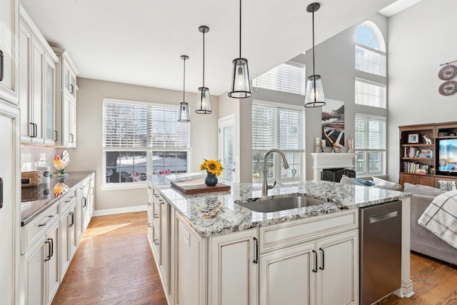 kitchen featuring sink, a center island with sink, light hardwood / wood-style flooring, stainless steel dishwasher, and pendant lighting