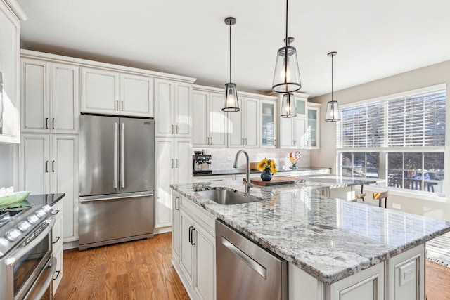 kitchen with white cabinetry, sink, hanging light fixtures, a kitchen island with sink, and stainless steel appliances