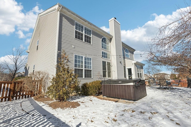 snow covered rear of property featuring a hot tub