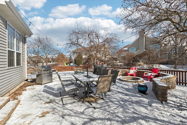 snow covered patio featuring area for grilling and a fire pit