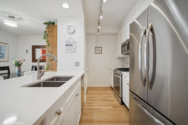 kitchen featuring light stone counters, appliances with stainless steel finishes, light wood-style floors, white cabinets, and a sink