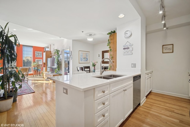 kitchen featuring light wood-style flooring, stainless steel dishwasher, white cabinetry, a sink, and a peninsula