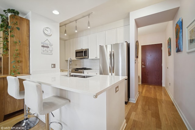 kitchen featuring stainless steel appliances, a breakfast bar, white cabinets, light countertops, and tasteful backsplash