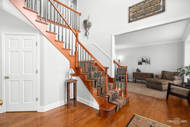 staircase with ornamental molding, a high ceiling, and hardwood / wood-style flooring