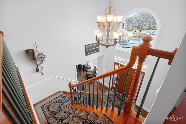 stairway with hardwood / wood-style floors, a towering ceiling, and a chandelier