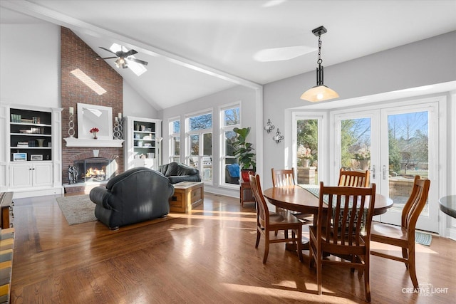 dining area featuring hardwood / wood-style flooring, french doors, a brick fireplace, ceiling fan, and vaulted ceiling with beams