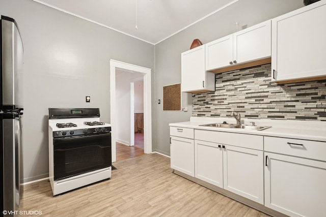 kitchen with white cabinets, gas range oven, sink, light hardwood / wood-style flooring, and backsplash