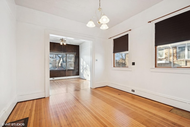 unfurnished room featuring a healthy amount of sunlight, ceiling fan with notable chandelier, and hardwood / wood-style flooring