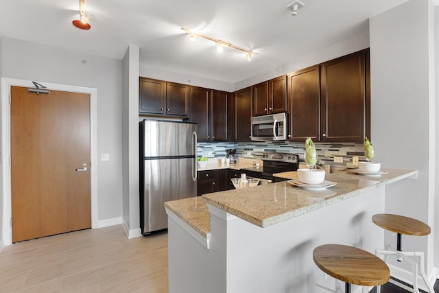 kitchen featuring light stone counters, kitchen peninsula, stainless steel appliances, tasteful backsplash, and a breakfast bar area