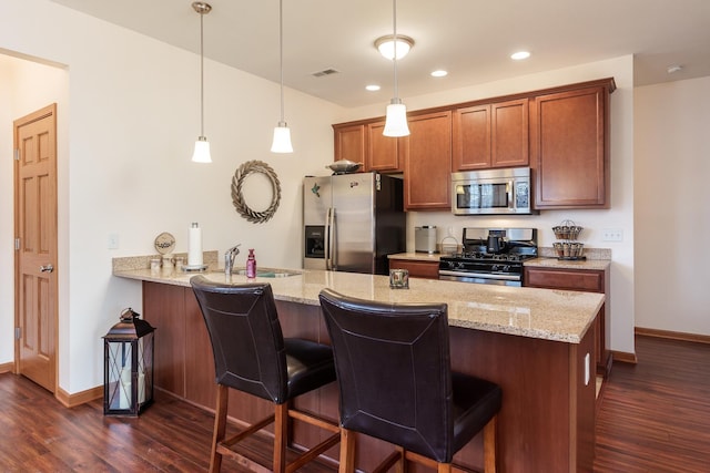 kitchen featuring kitchen peninsula, stainless steel appliances, pendant lighting, a breakfast bar, and sink