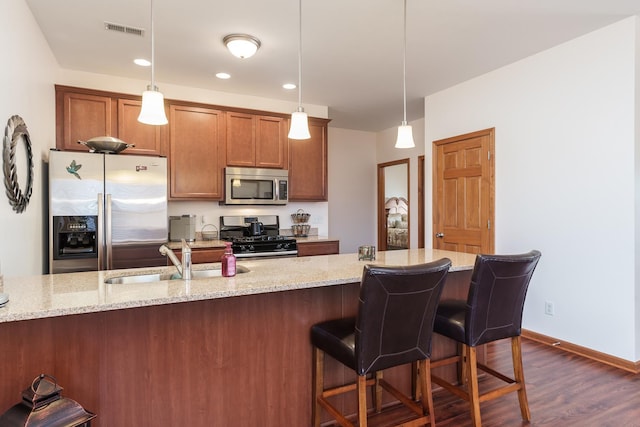 kitchen with stainless steel appliances, dark hardwood / wood-style floors, hanging light fixtures, light stone counters, and sink