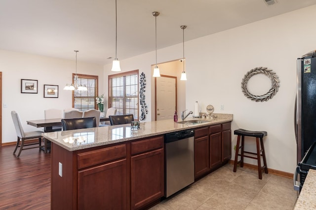 kitchen featuring kitchen peninsula, stainless steel appliances, pendant lighting, light stone counters, and sink