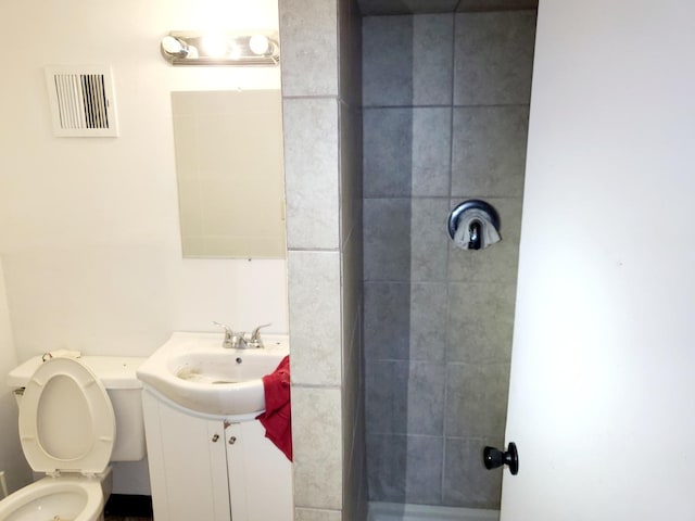 bathroom featuring a tile shower, vanity, and toilet