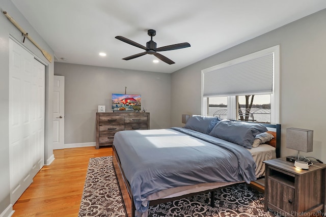 bedroom with ceiling fan, a closet, a barn door, and light hardwood / wood-style flooring