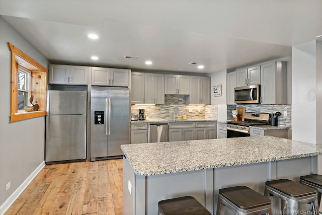 kitchen with appliances with stainless steel finishes, tasteful backsplash, light hardwood / wood-style floors, a kitchen breakfast bar, and gray cabinets