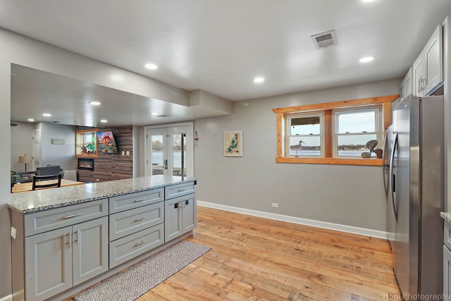 kitchen with light stone countertops, french doors, stainless steel refrigerator, gray cabinets, and light wood-type flooring