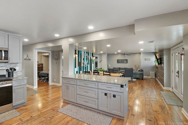 kitchen featuring stainless steel appliances, decorative backsplash, light wood-type flooring, a kitchen island, and light stone counters