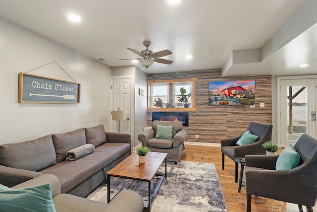 living room with ceiling fan, light wood-type flooring, and wooden walls