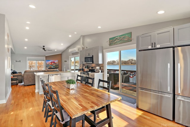 dining space featuring a water view, vaulted ceiling, plenty of natural light, and light hardwood / wood-style floors