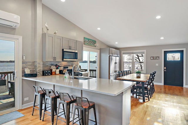 kitchen featuring stainless steel appliances, backsplash, kitchen peninsula, a water view, and gray cabinetry