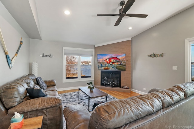 living room featuring lofted ceiling, ceiling fan, a brick fireplace, and light hardwood / wood-style floors