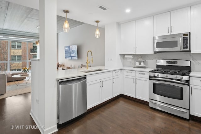 kitchen with sink, appliances with stainless steel finishes, white cabinetry, hanging light fixtures, and decorative backsplash