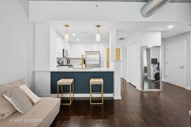 kitchen with dark wood-type flooring, white cabinetry, appliances with stainless steel finishes, kitchen peninsula, and pendant lighting