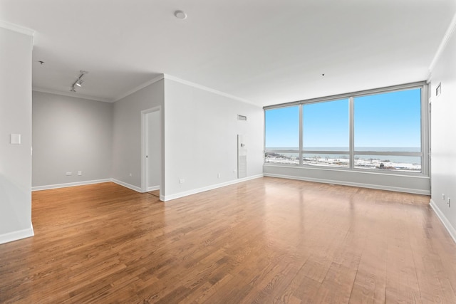 empty room featuring light wood-type flooring, a water view, crown molding, and rail lighting