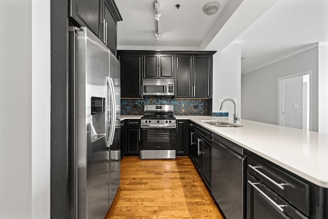 kitchen with sink, light hardwood / wood-style flooring, kitchen peninsula, backsplash, and appliances with stainless steel finishes