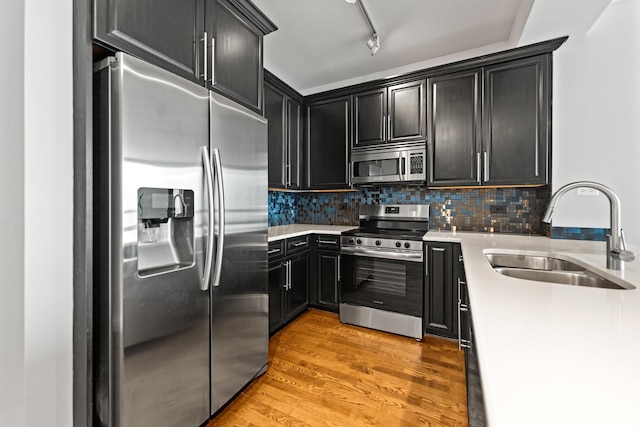 kitchen with rail lighting, appliances with stainless steel finishes, light hardwood / wood-style floors, sink, and backsplash