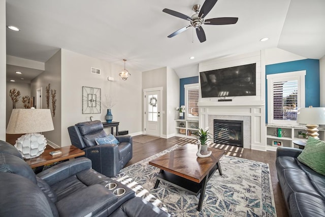 living room with a fireplace, vaulted ceiling, built in features, ceiling fan with notable chandelier, and dark wood-type flooring