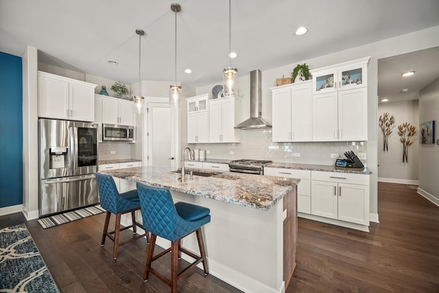 kitchen with decorative light fixtures, a center island with sink, wall chimney range hood, appliances with stainless steel finishes, and sink