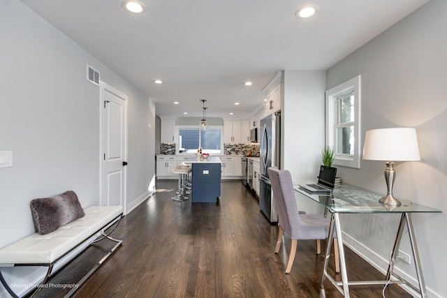 interior space featuring hanging light fixtures, a kitchen island, stainless steel refrigerator, white cabinets, and a kitchen breakfast bar