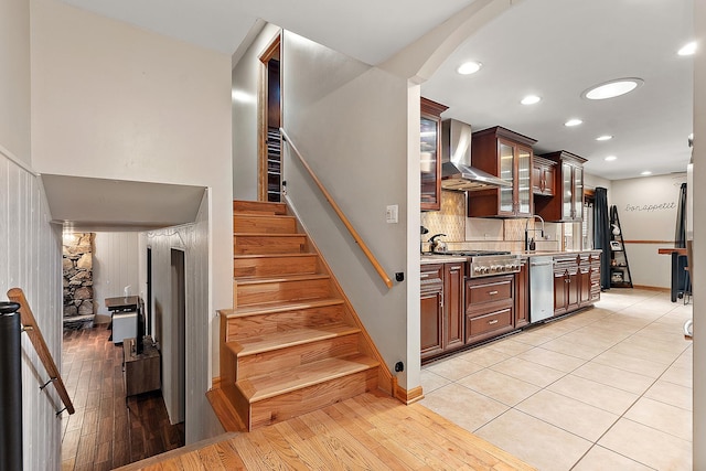 kitchen featuring light stone countertops, wall chimney exhaust hood, light hardwood / wood-style flooring, stainless steel appliances, and dark brown cabinets