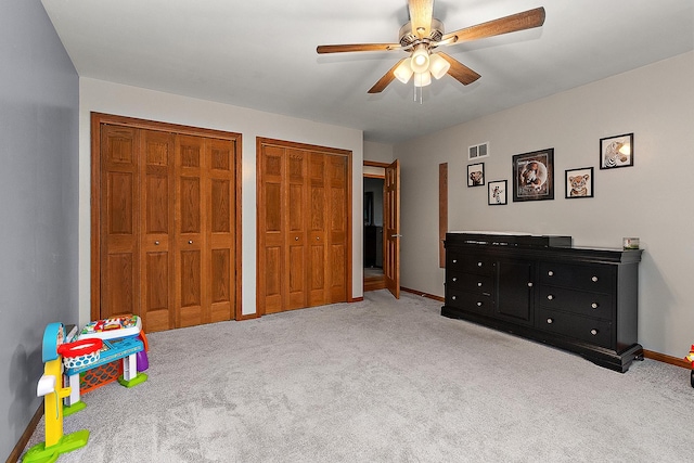 bedroom featuring light carpet, ceiling fan, and two closets