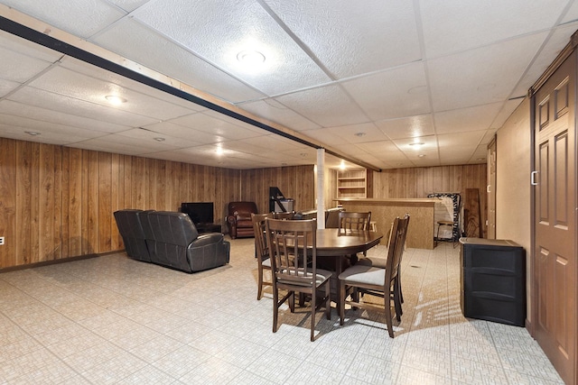 dining space featuring wood walls and a drop ceiling