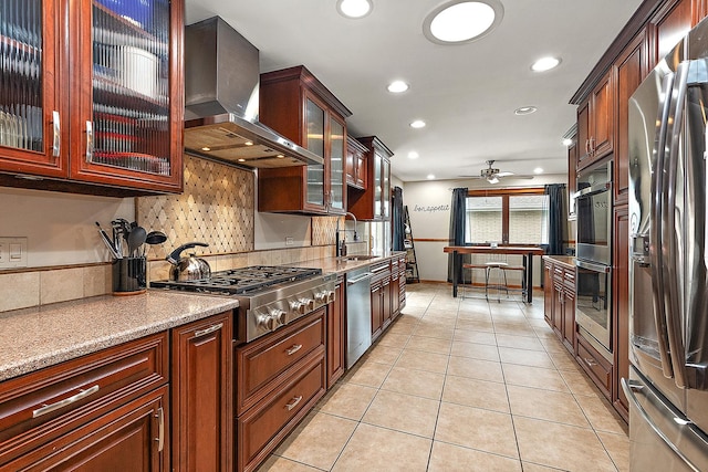 kitchen featuring stainless steel appliances, wall chimney exhaust hood, ceiling fan, light tile patterned floors, and light stone countertops