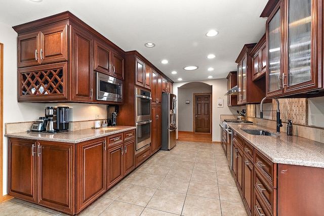 kitchen with appliances with stainless steel finishes, light tile patterned flooring, light stone countertops, and sink